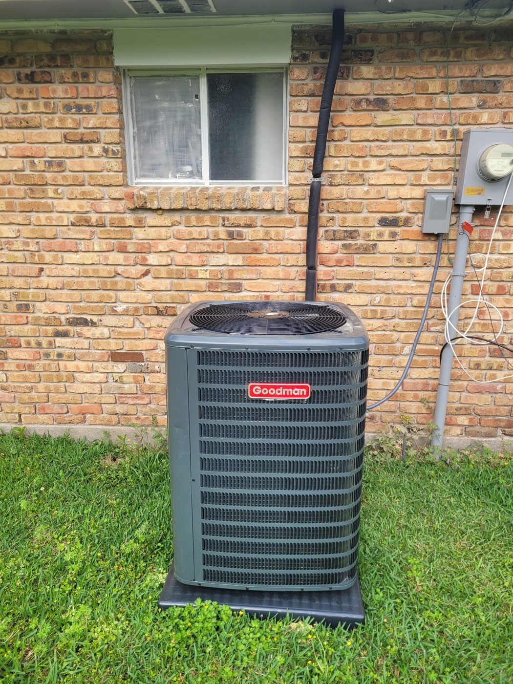 New Goodman condenser installed beside a brick home